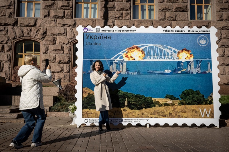 Ουκρανοί φωτογραφίζονται με φόντο απεικόνιση της έκρηξης στη γέφυρα
